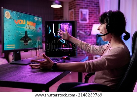 Young gamer celebrating video games championship win on online live stream, feeling happy at desk with neon lights. Female streamer winning shooter gaming tournament on computer. Royalty-Free Stock Photo #2148239769