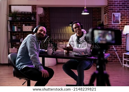 Male influencer using camera to record podcast conversation, filming talking show discussion in studio. Social media vlogger chatting and broadcasting live, meeting with happy guest. Royalty-Free Stock Photo #2148239821