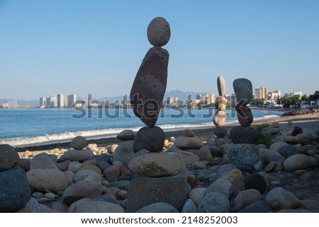 Rocks stacked on top of each other standing vertically at a beach, blue water, city skyline, sky out of focus in the background. Balance, harmony, relaxation and peace concept. Space for copy.