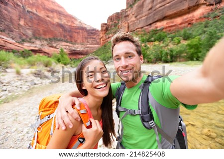 Travel hiking selfie self-portrait photo by happy couple on hike. Active lifestyle with hikers friends or lovers smiling at camera in Zion National Park, Utah, USA. Young Asian woman and Caucasian man