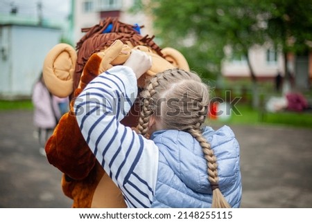 Child plays with growth doll. Animator at festival entertains children. Girl holds man in monkey costume. Rest in park. Details of scene.
