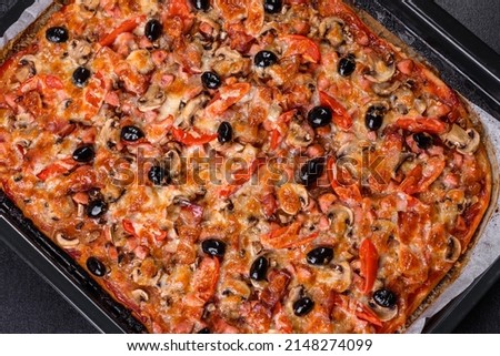 Small homemade vegetable pizza with addition of tomatoes, olives and herbs on a dark conkrete table