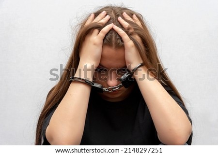 A young girl handcuffed on a gray background, close-up. Juvenile delinquent in a black T-shirt, criminal liability of minors. Royalty-Free Stock Photo #2148297251