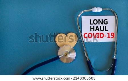 COVID-19 long-haul covid symptoms symbol. White card with words Long haul covid-19. Wooden heart, stethoscope, beautiful blue background copy space. Medical, COVID-19 long-haul covid symptoms concept.