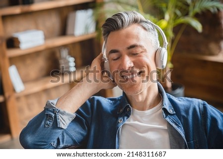 Relaxed caucasian mature middle-aged man freelancer listening to the music song playlist radio podcast in headphones earphones in mobile application online at home office Royalty-Free Stock Photo #2148311687