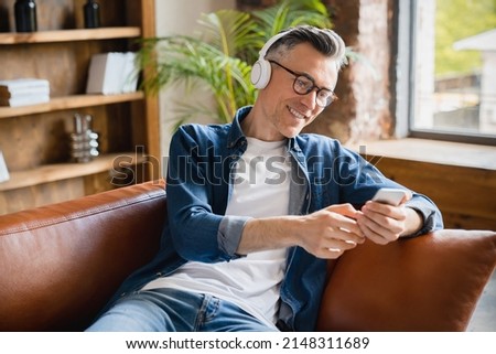Smiling caucasian mature middle-aged man freelancer relaxing resting listening to the music radio podcast playlist choosing soundtrack on cellphone at home office Royalty-Free Stock Photo #2148311689