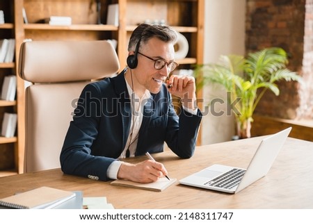 E-learning, distant education. Caucasian middle-aged mature businessman ceo boss freelancer teacher psychologist writing, taking notes while on online lesson session videocall in office Royalty-Free Stock Photo #2148311747