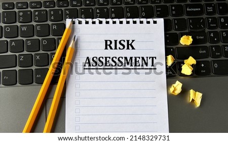 RISK ASSESSMENT - words in a white notepad on the background of a laptop with pencils. Business concept