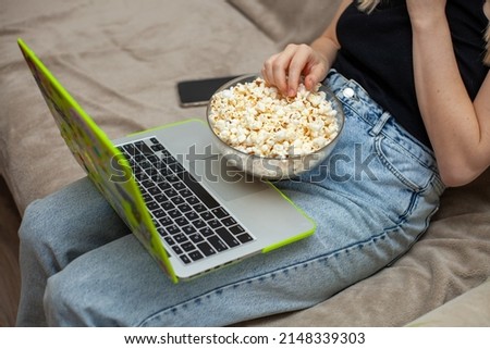 a bowl of popcorn on the legs of a girl next to a laptop watching a movie