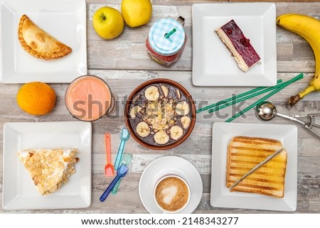 Top view image of breakfast plate, coffee, empanadas, cakes, fresh fruits, acai and mixed sandwich