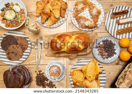 Top view image of desserts, brioche bread, chocolate palm trees, apple pie, cookies, oranges, butter croissants and salad