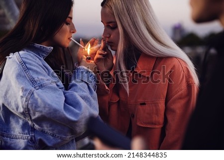 Two rebellious teenage girls lightning cigarettes and smoke. Teenagers smoking cigarettes Royalty-Free Stock Photo #2148344835