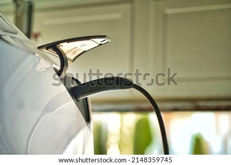White EV electric car plugged and charging inside garage at home. Home EV charger station is very convenient for customer refuelling battery with less cost compare to supercharger station. Royalty-Free Stock Photo #2148359745