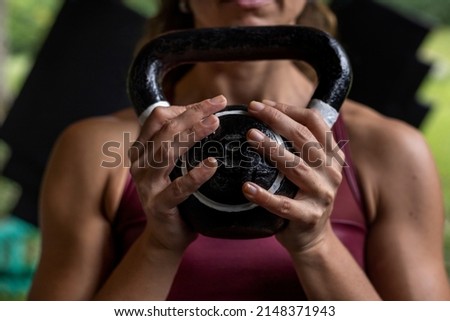 Unrecognizable Latin American woman holds a kettlebell with both hands during her high intensity functional workouts at the gym. Healthy lifestyle concept.