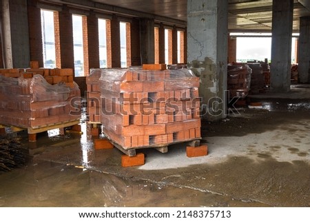 Pallets of bricks stand inside a monolithic frame building under construction waiting for masons to erect brick walls, selective focus