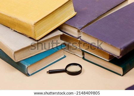 World book daу. A stack of books with a magnifying glass highlighted on a beige background. Search for information.