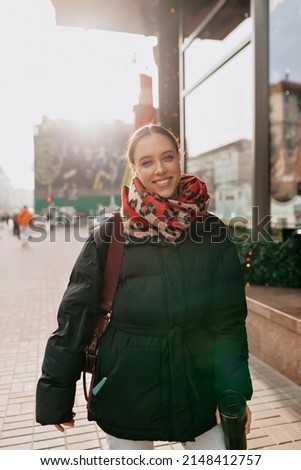 Lovely young lady with brunette hair in stylish jacket and scarf with bag , standing on old european street in sunlight and sensitively posing outdoors. Warm autumn