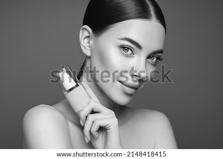 Portrait beautiful young woman with clean fresh skin. Model with foundation makeup bottle. Cosmetology, beauty and spa. Black and White photo