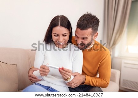 Enamoured couple finding out results of a pregnancy test sitting on the bed. Happy couple checking pregnancy test sitting on a couch in the living room at home. Family, parenting and medical concept Royalty-Free Stock Photo #2148418967