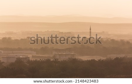 Sunset in Siwa. Yellow sky because of  dust and sand in the air and silhouettes of local houses and a mosque. Layers of hills and mountains. Egypt