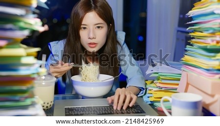 asian young businesswoman is eating instant noodles and tapioca ball milk tea with laptop computer while overworking in office at night