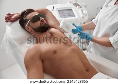 Man with goggles and bare chest undergoes procedure of arm pit laser epilation in clinic Royalty-Free Stock Photo #2148429855