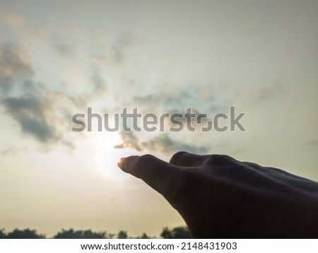photo of a finger pointing at the sun silhouette