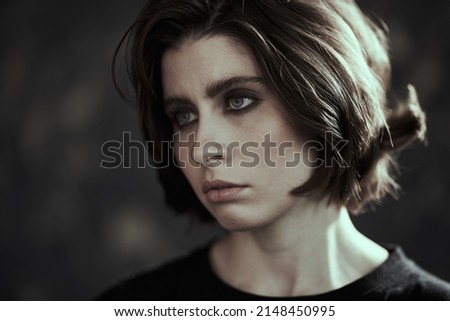 Close up shot of a brunette girl with dramatic dark eye makeup looking away with an expression of tiredness and emptiness in her eyes. Psychological picture. People, emotions.