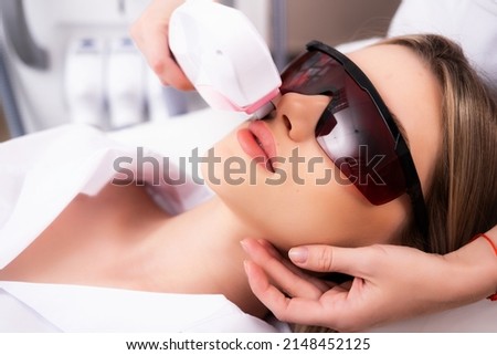Facial hair removal. Photo of a woman patient in glasses receiving a laser hair removal procedure. Apparatus for depilation. Royalty-Free Stock Photo #2148452125