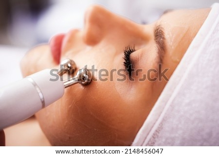 Close-up portrait of a beautiful woman with closed eyes and apparatus for skin rejuvenation. Beauty salon procedures. RF lifting. Microcurrents. Royalty-Free Stock Photo #2148456047