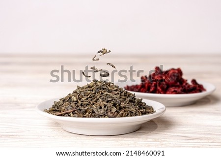 green tea and dried cranberries lie in saucers on a white wooden background, copy space