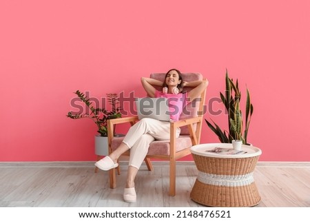Young woman with laptop sitting in comfortable armchair at home