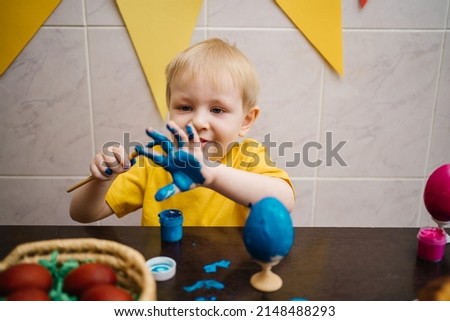 little boy draws blue paint on his hand, paints an Easter egg. High quality photo