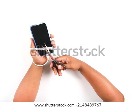 One hand of a man holding a smartphone is wrapped by a charger cable and cut with scissors.Social Disease and smart phone addiction concept white background isolated.with clipping path