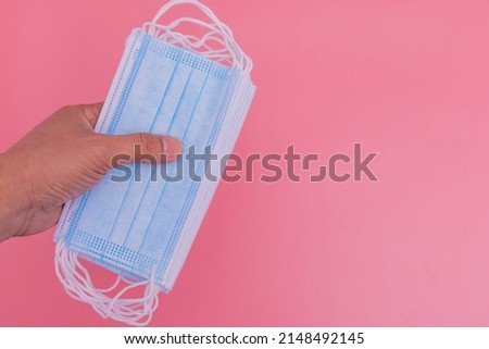 Hand holding a blue mask on a pink background