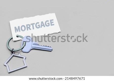 The concept of mortgage, sale and rental of housing and real estate. Mortgage credit lending. Keychain in the shape of a house with a key on a gray background