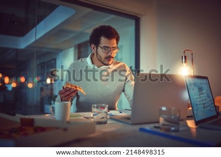 Getting some energy for another late night. Shot of a young designer eating pizza while working late in an office. Royalty-Free Stock Photo #2148498315
