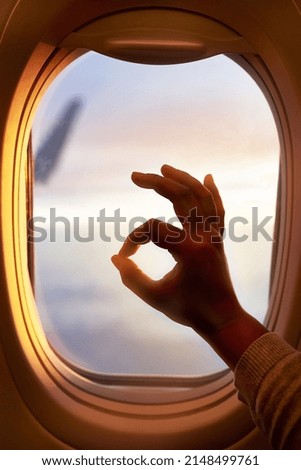 This flight is going just fine. Shot of a passenger making an okay sign while looking through the window of an airplane.