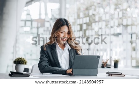 A businesswoman is checking company financial documents and using a tablet to talk to the chief financial officer through a messaging program. Concept of company financial management. Royalty-Free Stock Photo #2148504957