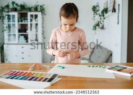 A little girl studies at home, modellng from plasticine. Little girl sculpts figures, make spring from plasticine art on paper. Art therapy for children