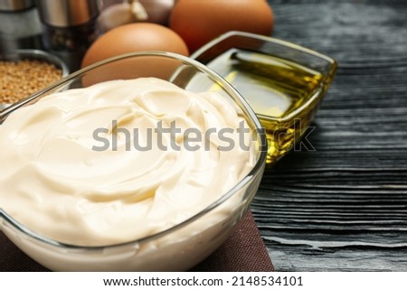 Glass bowl with fresh mayonnaise on black wooden table, closeup. Space for text