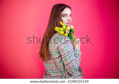 Happy young woman with bouquet of tulips on pink background.