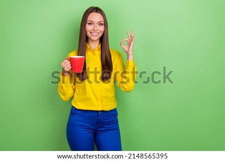 Portrait of attractive cheerful girl employee drinking caffeine showing ok-sign isolated over green pastel color background
