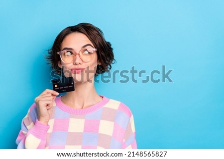 Photo of thinking young brunette lady hold card look empty space wear eyewear plaid pullover isolated on blue background