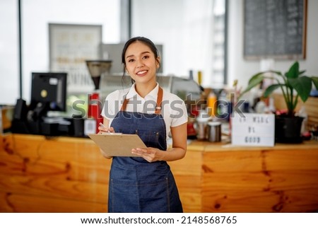 Opening a small business, AHappy Asian woman in an apron standing  near a bar counter coffee shop, Small business owner, restaurant, barista, cafe, Online, SME, entrepreneur, and  seller concept Royalty-Free Stock Photo #2148568765