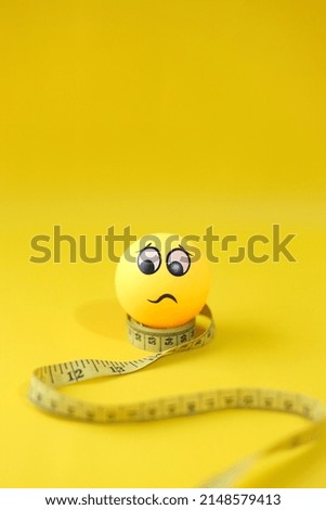 Yellow measuring tape with worried emoticon isolated on yellow background. Creative flat lay, copy space for diet and healthy lifestyle. 