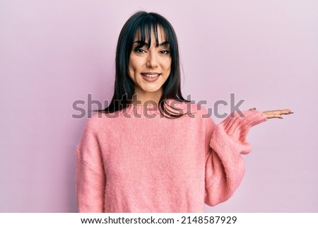 Young brunette woman with bangs wearing casual winter sweater smiling cheerful presenting and pointing with palm of hand looking at the camera. 