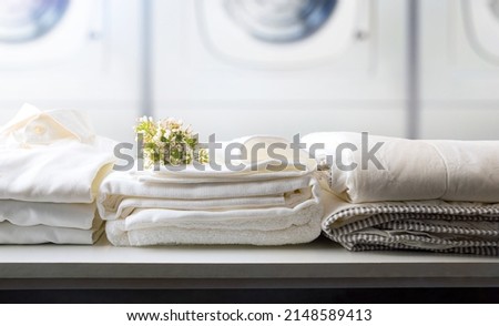 Self-service laundry for the public with bedding and staff on a white bench and professional washing machines in the background. Front view. Horizontal composition. Royalty-Free Stock Photo #2148589413