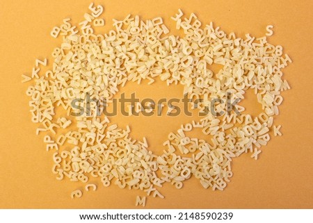Whole grain dark pasta letters on dark yellow textured background with selected focus