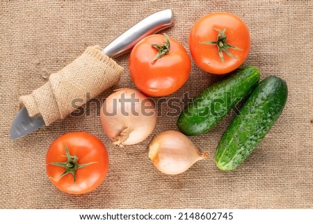 Three ripe tomatoes, two onions and two cucumbers on jute fabric, macro, top view.